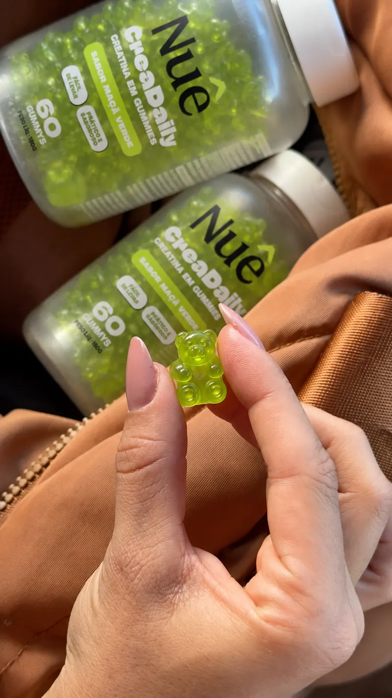 Dois potes de CreaDaily dentro de uma bolsa e uma goma verde de ursinho entre os dedos