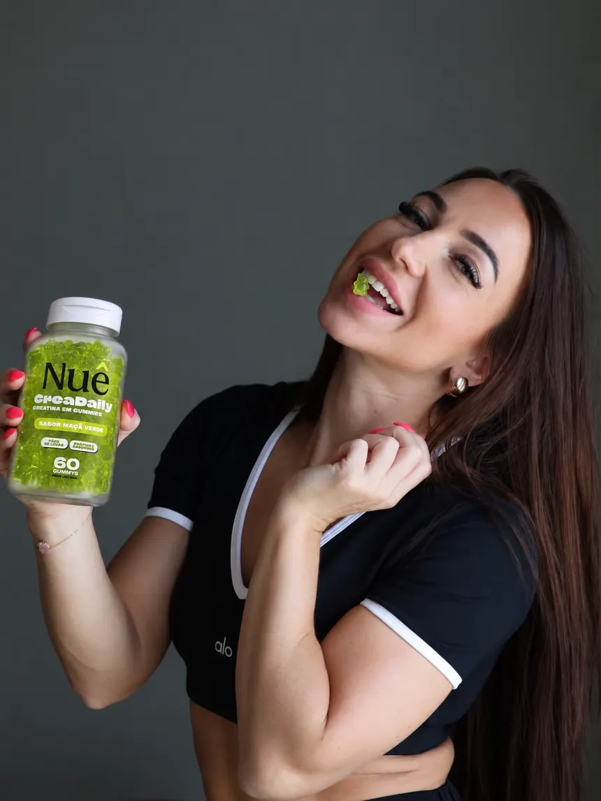 Mulher com roupa de treino sorrindo com uma goma entre os dentes e o pote de CreaDaily na mão